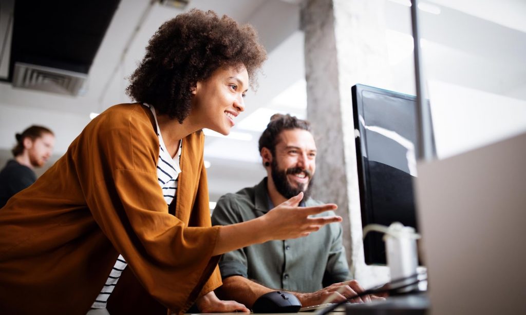 A woman and man sitting at a desk with a computer.